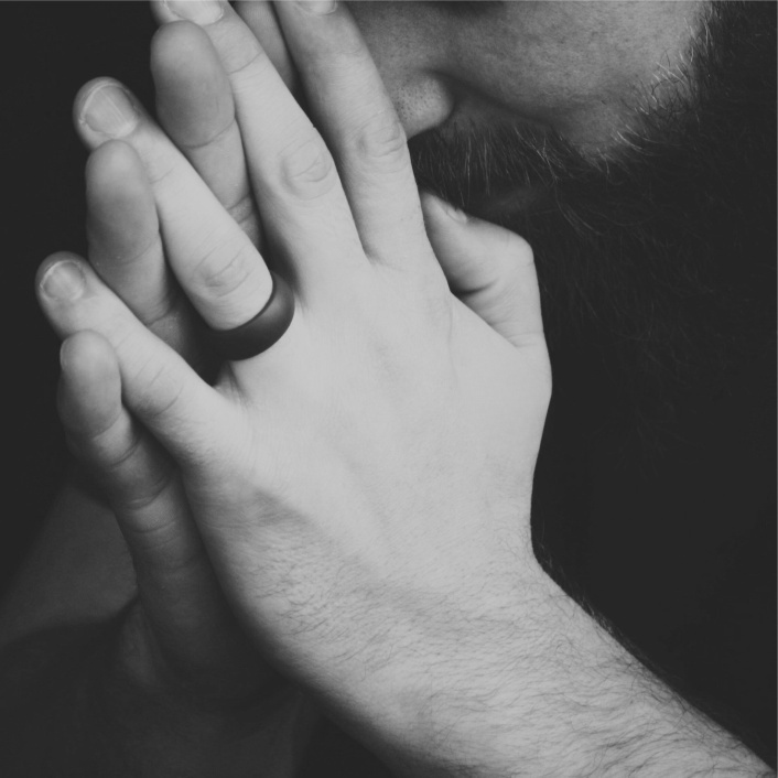 man's hands with a black ring folded in prayer
