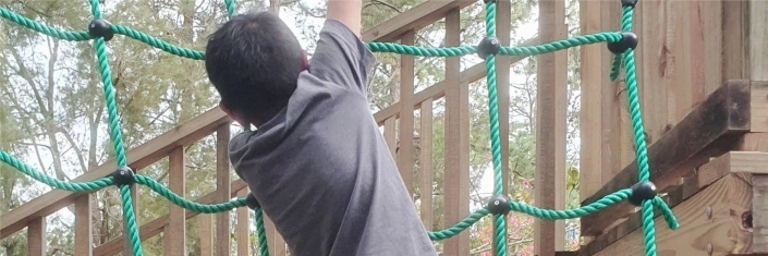 A young boy climing ropes in playground.