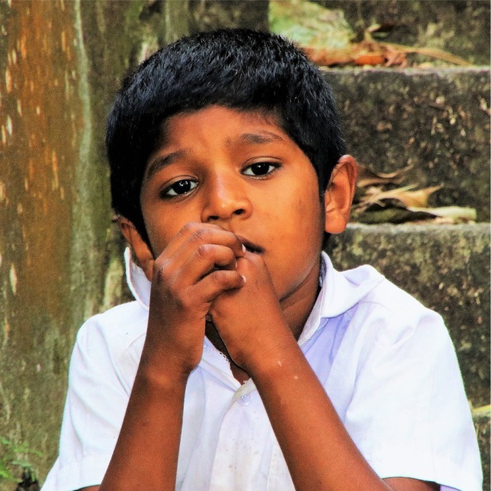 Young boy looking seriously into camera with hands to face.