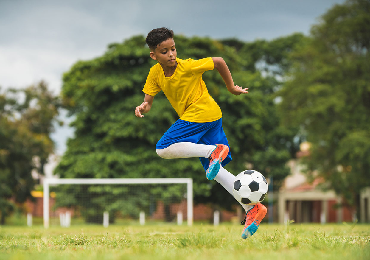 Un jeune joueur de soccer s’élance et saisit le ballon rond avec ses pieds.