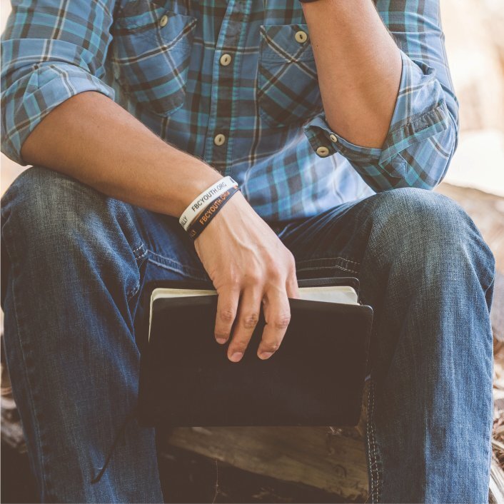 Man in blue plaid shirt and blue jeans, holding black Bible in his hand, sitting in prayer