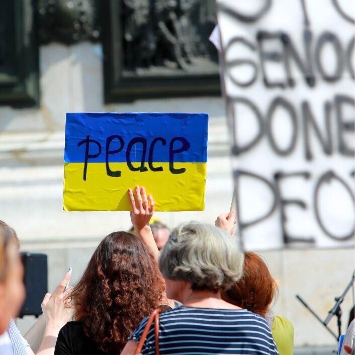 The word 'peace' on the backdrop of the Ukrainian flag a woman is holding up in the midst of a crowd