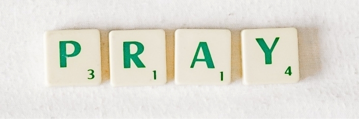 The word PRAY spelled out in Scrabble tiles laying on a white fabric sheet