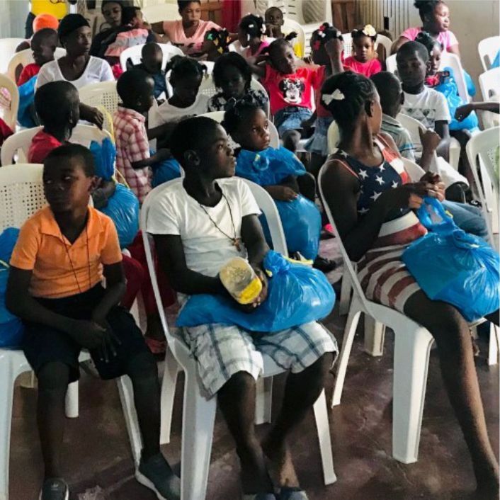 Group of Haitian children sitting with bags of food and supplies for their families.