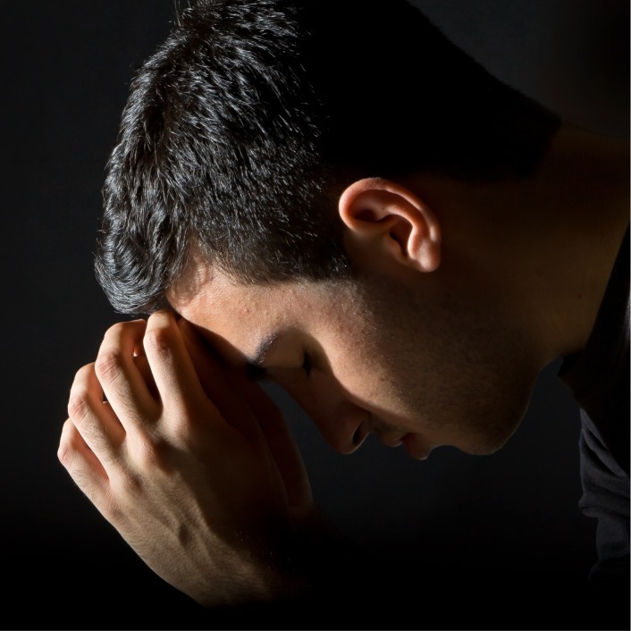 Head and shoulders of a dark-haired man with head bowed praying.