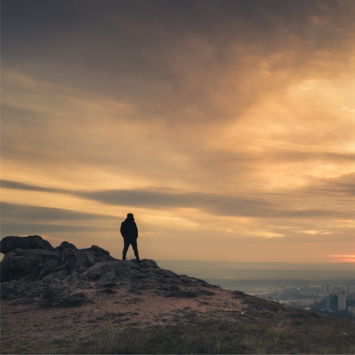 Sunset backdrop silhouette of a man standing on a hill overlooking a city