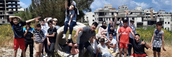 Group of middle eastern children and youth playing together outside with buildings in background.