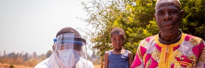 African doctor working outdoors wearing face shield while with two patients