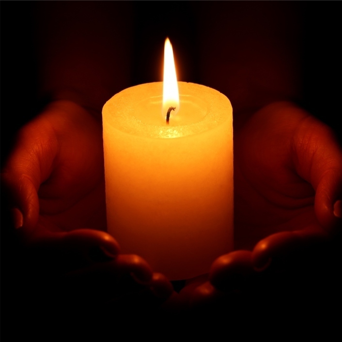 A pair of hands holding a thick lit candle