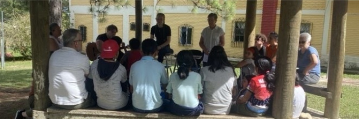Group of children and adults gathered for worship under an outdoor covering